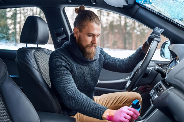 Ein Mann sitzt in einem Auto und reinigt den Autoinnenraum mit den speziellen Reinigern von Koleen.